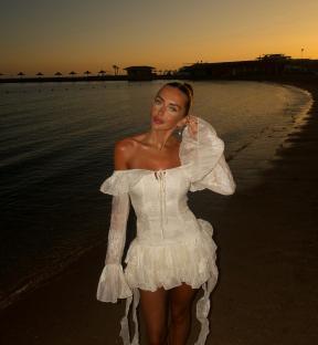 Woman in white dress on beach at sunset.