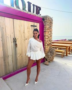 Woman in white outfit standing in front of a pink building.