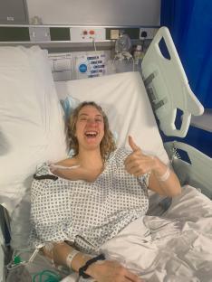 Woman in hospital bed giving thumbs up.