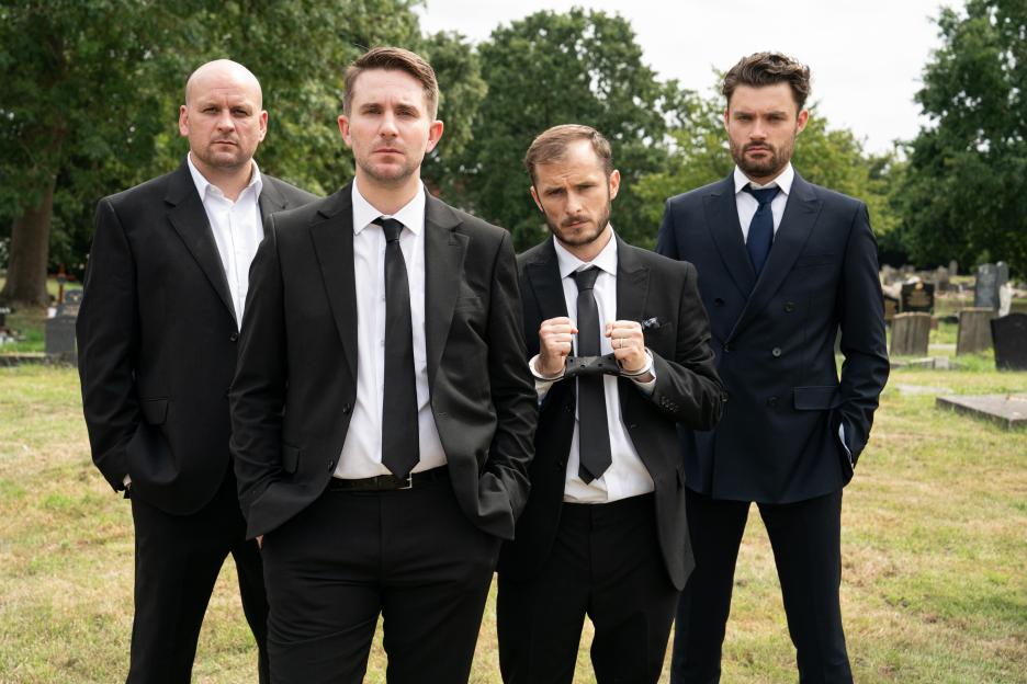 Four men in suits at a cemetery.