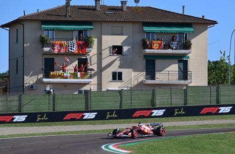 Formula 1 race car driving past spectators on balconies waving flags.
