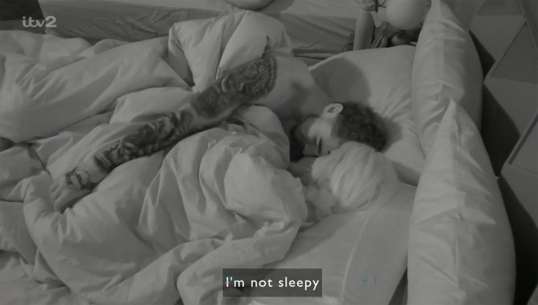 Two people under covers in a bed from Big Brother Day 3, with the text "I'm not sleepy" on screen.