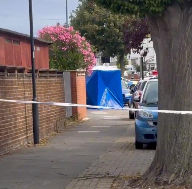 Crime scene in Wembley, UK. A blue forensic tent is visible behind police tape.