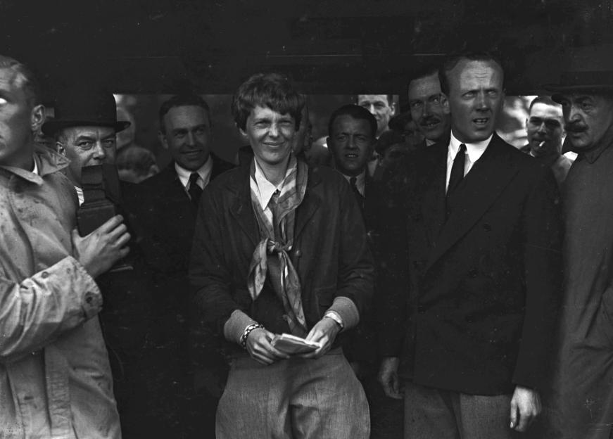 Amelia Earhart smiles in a crowd of men after her solo transatlantic flight.