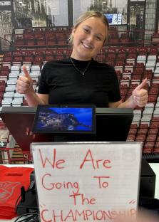 Young woman working at Wrexham AFC souvenir shop giving thumbs up; sign says
