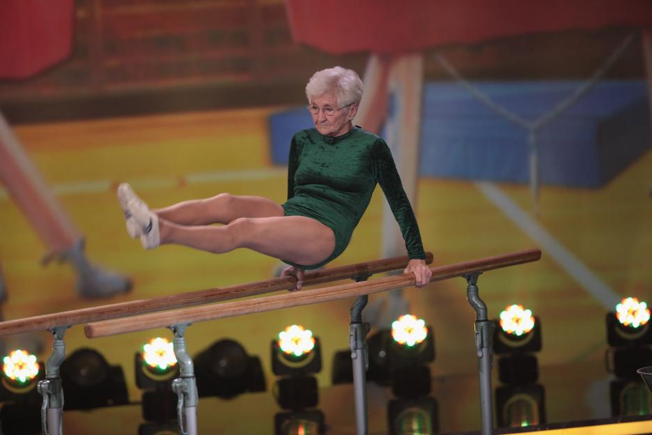 Elderly woman performing gymnastics on parallel bars.