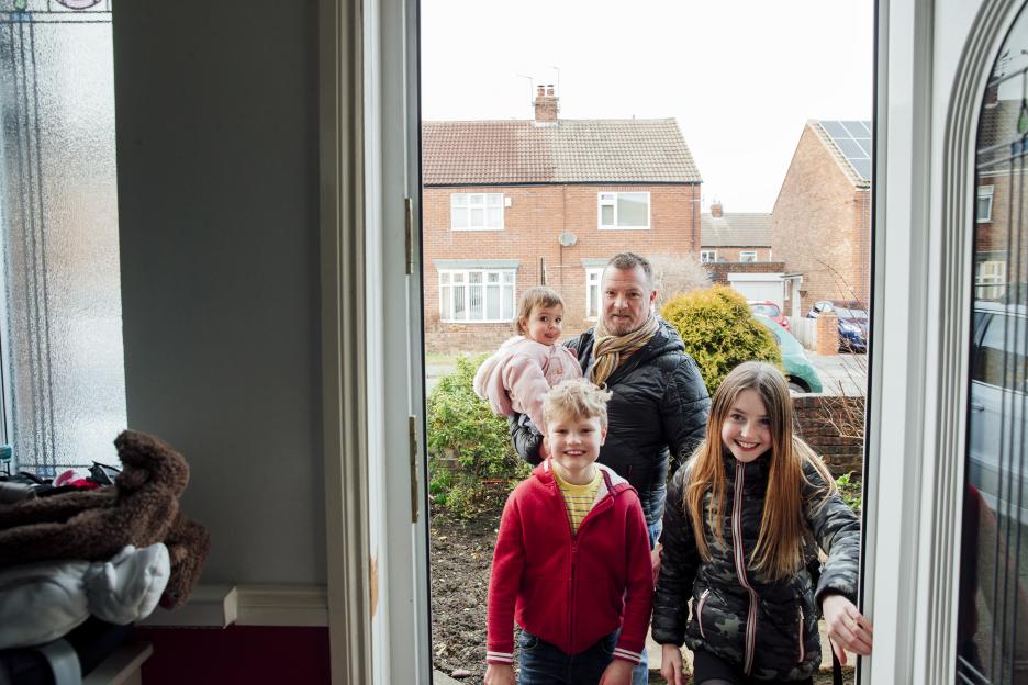 A father and his three children arrive home and enter through the front door.