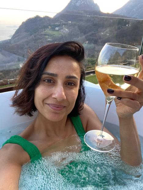 Woman in a hot tub with a glass of wine, overlooking a mountain view.