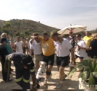 A strongman with a leg injury being helped by others.