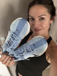 Person holding up a pair of light blue Nike running shoes.