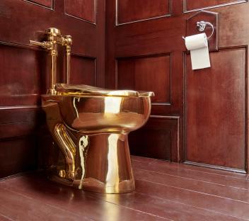Gold toilet sculpture in a wood-paneled room.