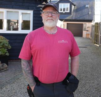 A man wearing a pink shirt stands outside a house.