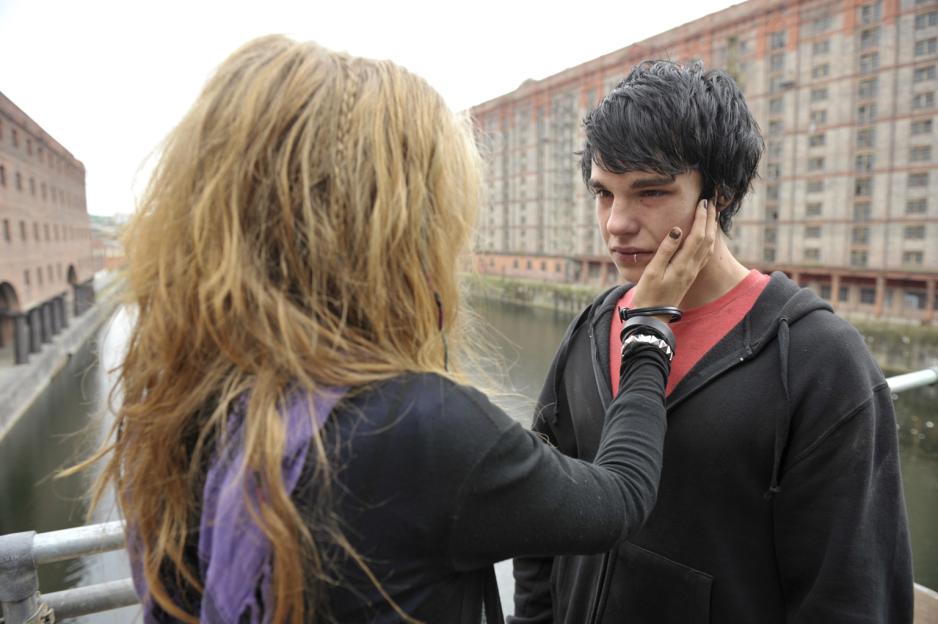 A young woman comforts a young man by the water.