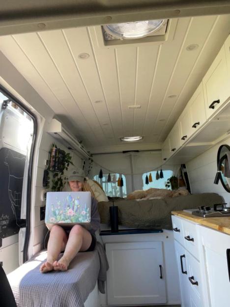 Woman working on laptop inside camper van.