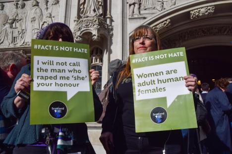 Two women holding signs outside the Supreme Court protesting the legal definition of woman.