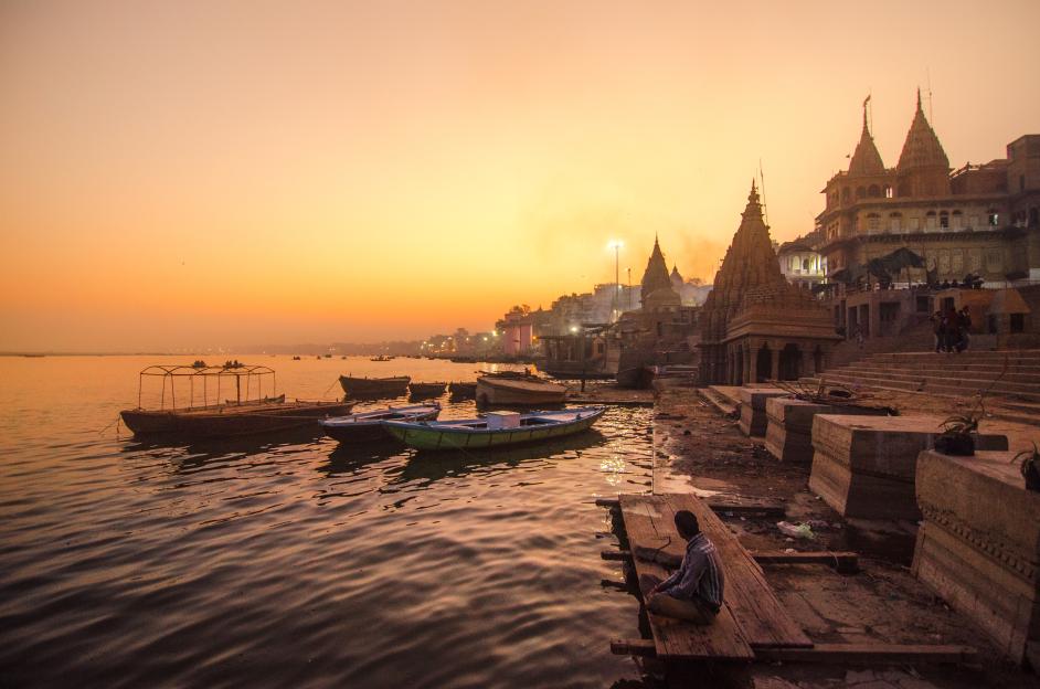A man is resting at the burning ghats of Varanasi, India, as the sun sets over the Ganges River.