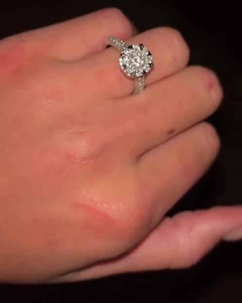 A close-up of a hand wearing a sparkling engagement ring.