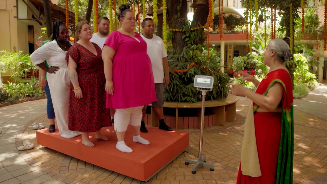 Group of people standing on a scale with a woman instructing them.