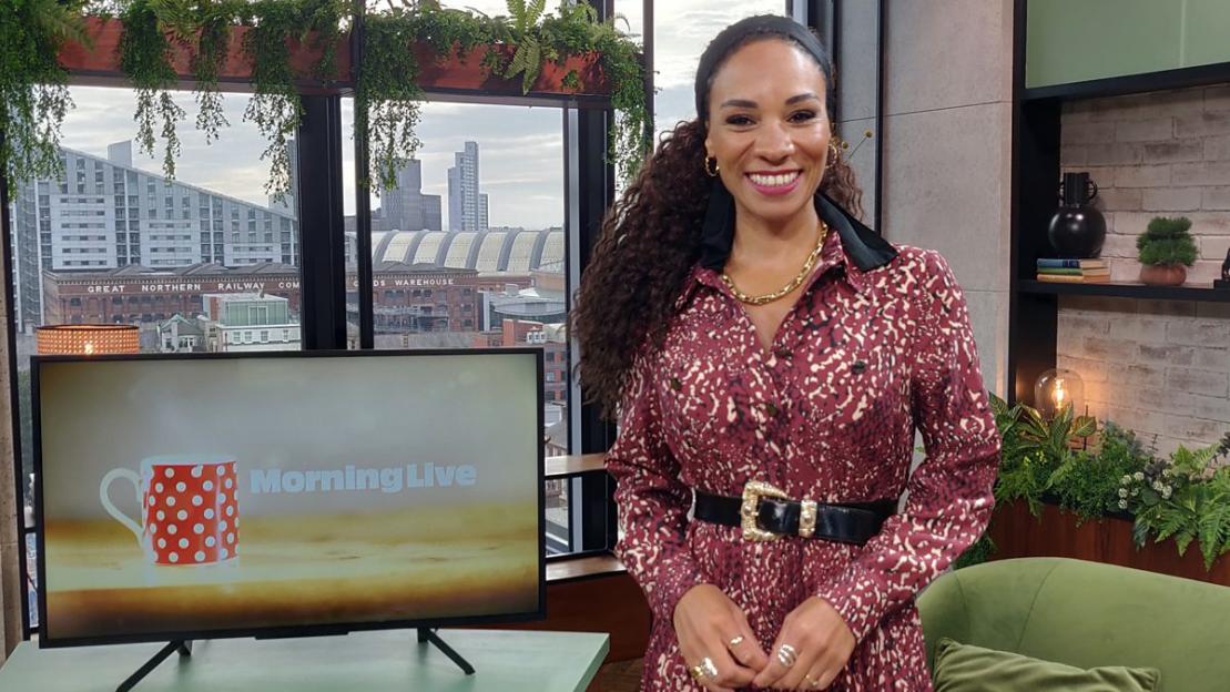 Michelle Ackerley smiling in a studio with "Morning Live" on a screen to her left.