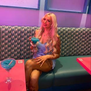 Woman sitting on a teal booth, holding a blue cocktail.
