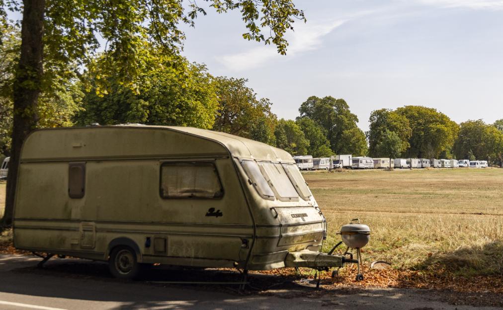 A caravan parked near a row of vans on a grassy field.