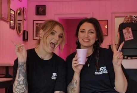 Two women in a pink cafe, one holding a cup.