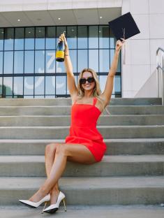 Woman in red dress celebrating graduation with champagne and cap.