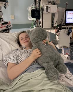 Teenage girl in hospital bed holding stuffed animal.