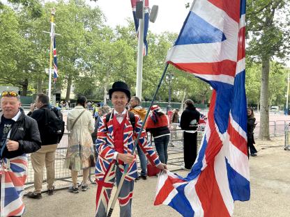Man in Union Jack suit holding a large Union Jack flag outside Buckingham Palace.