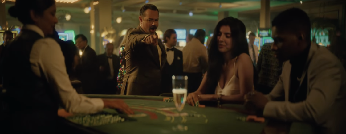 A man in a suit points angrily at a woman at a casino table.