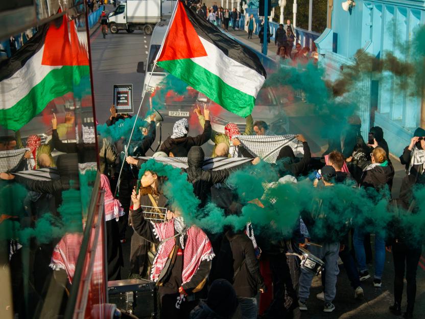 Protesters blocking Tower Bridge with Palestinian flags and green smoke flares.