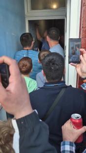A crowd of people gathered outside a doorway, one person is writing on the door.