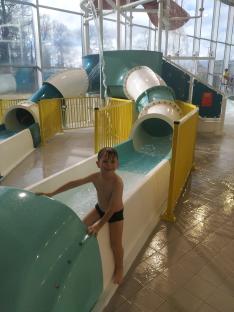 Boy sitting on a water slide at an indoor water park.