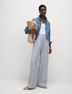 Woman wearing linen-rich wide-leg trousers, denim jacket, and white top.
