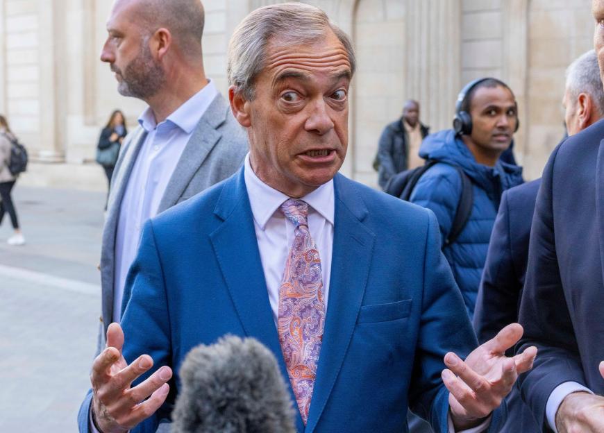 Nigel Farage speaking with animated gestures into a microphone, with Richard Tice behind him.