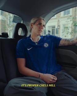 A woman in a Chelsea FC jersey sits in a car.