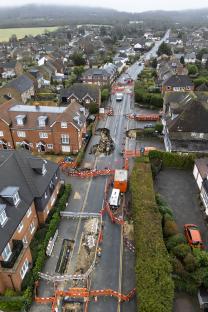 Aerial view of sinkholes in a residential street, surrounded by barriers and emergency vehicles.