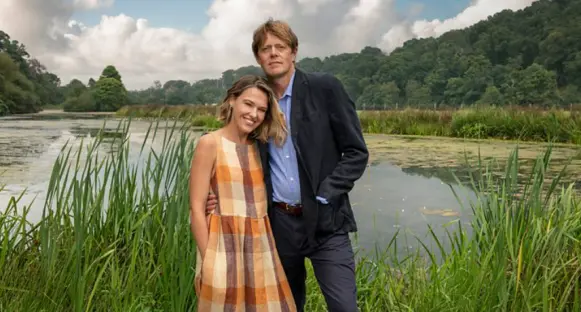 A couple stands by a lake.