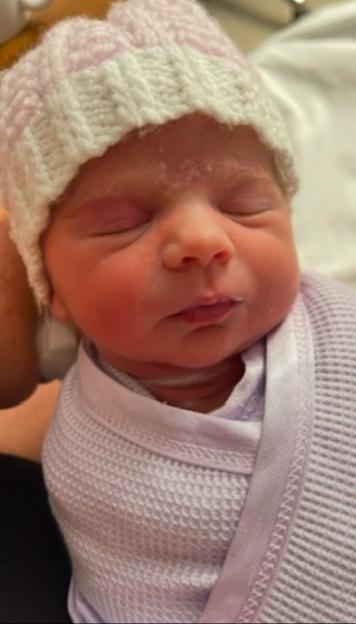 Newborn baby Teraysa wrapped in a purple blanket, wearing a pink and white knitted hat.