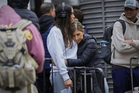 Two women embrace at a train station while waiting for news about delayed trains.