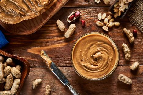 Peanut butter on toast, in a bowl, and peanuts on a wooden table.