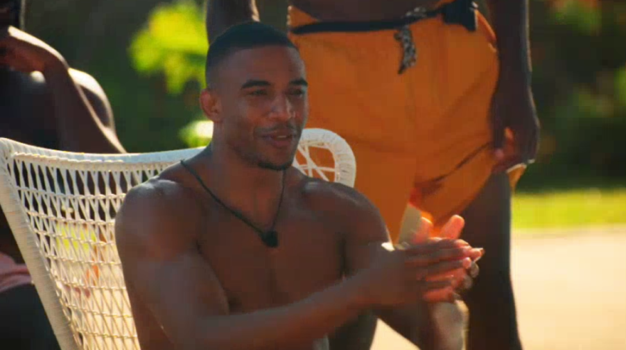 A man in a reality show setting, wearing only shorts, claps his hands.