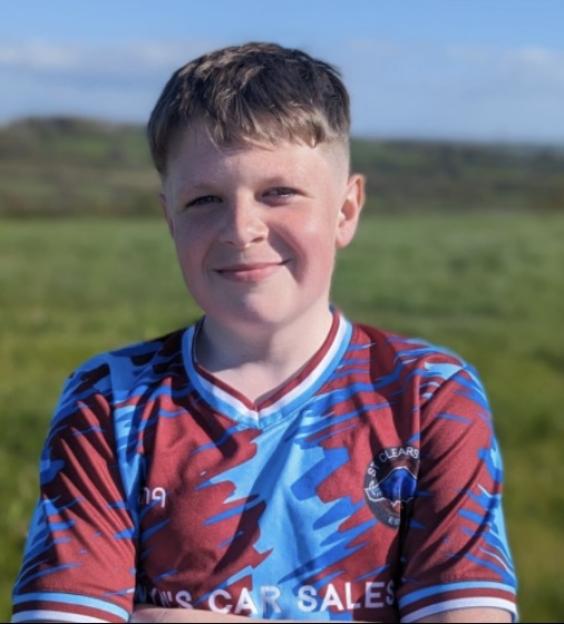Leon Arundel, a young boy in a blue and red sports jersey, stands in a grassy field.