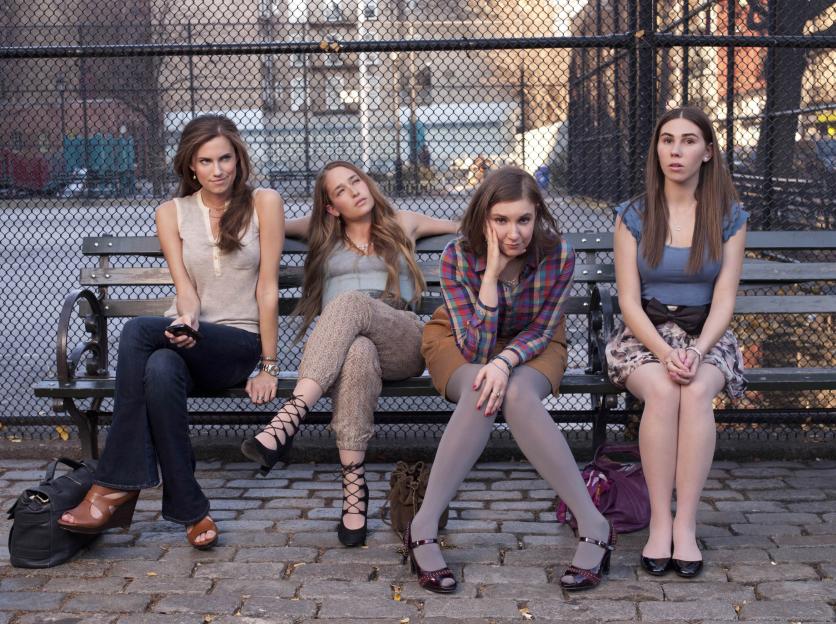 Allison Williams as Marnie, Jemima Kirke as Jessa, Lena Dunham as Hannah, and Zosia Mamet as Shoshanna from the TV series "Girls", sitting on a park bench.
