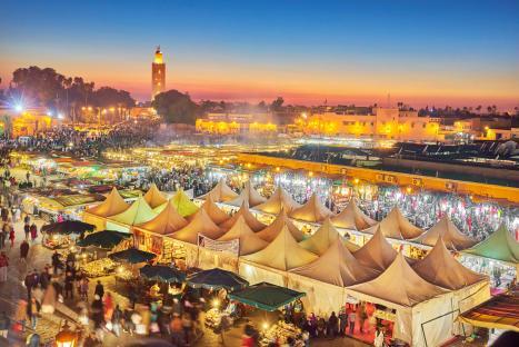 Djemaa el-Fna square in Marrakech at dusk, with many market stalls and people.
