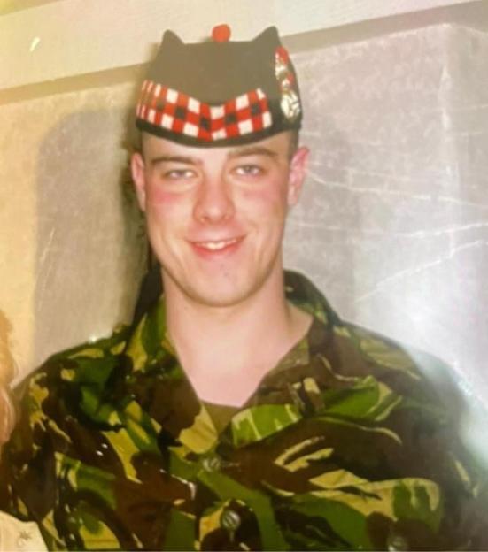 Dave Stewart, 40, when he was in the army, wearing camouflage and a black hat with red and white plaid.