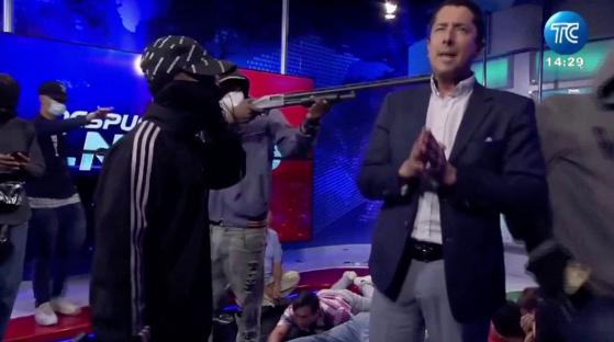 Screengrab of a man pointing a shotgun at a television presenter during a live broadcast.