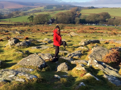 Person in red jacket and dog walking across a rocky field.