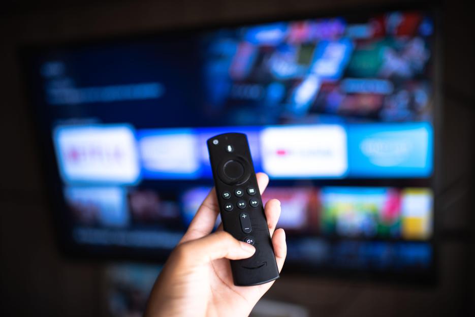 Hand holding Amazon Fire TV Stick remote in front of a TV screen.