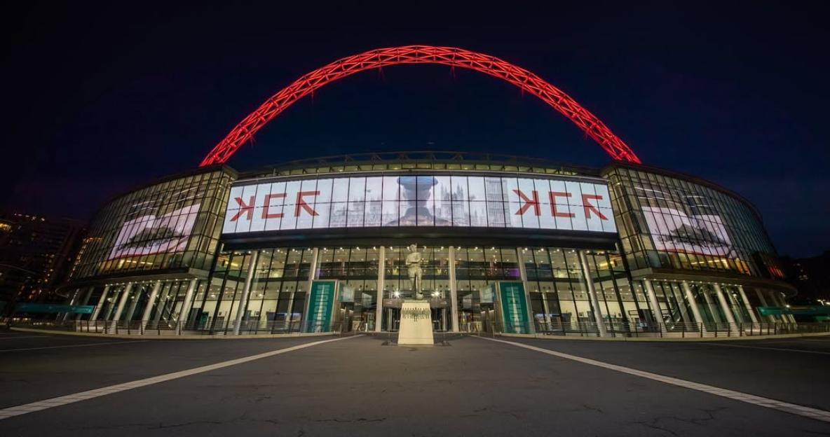 Wembley Stadium at night with a large screen displaying a band's name.